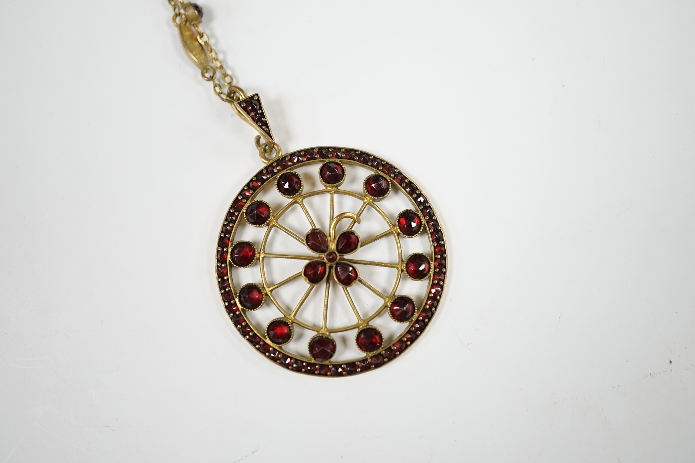 A late Victorian gilt metal and garnet cluster set 'wheel' pendant on a garnet set chain, overall 48cm. Condition - poor to fair